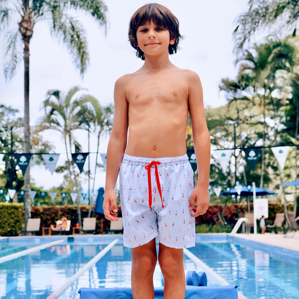 Young boy standing on a diving board by a pool with palm trees in the background