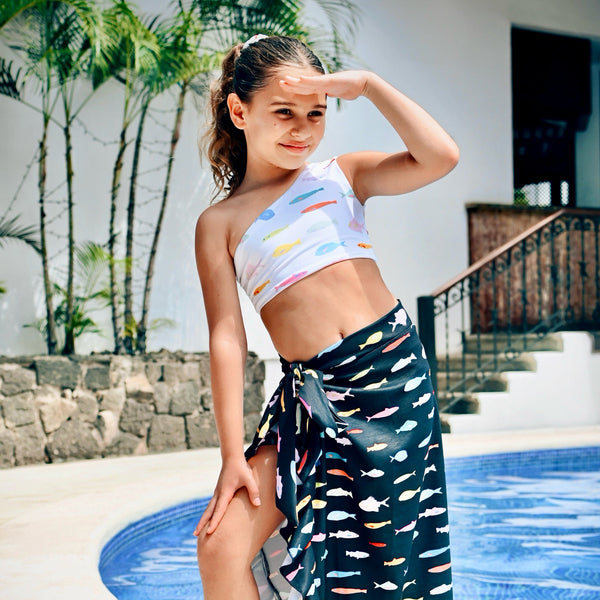 Young girl in a colorful top and patterned sarong by a poolside.